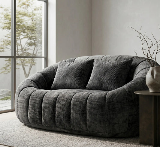 Gros plan détaillé sur le tissu texturé et les plis d'un canapé pouf gris anthracite foncé, montrant la qualité du tissage près d'une fenêtre.