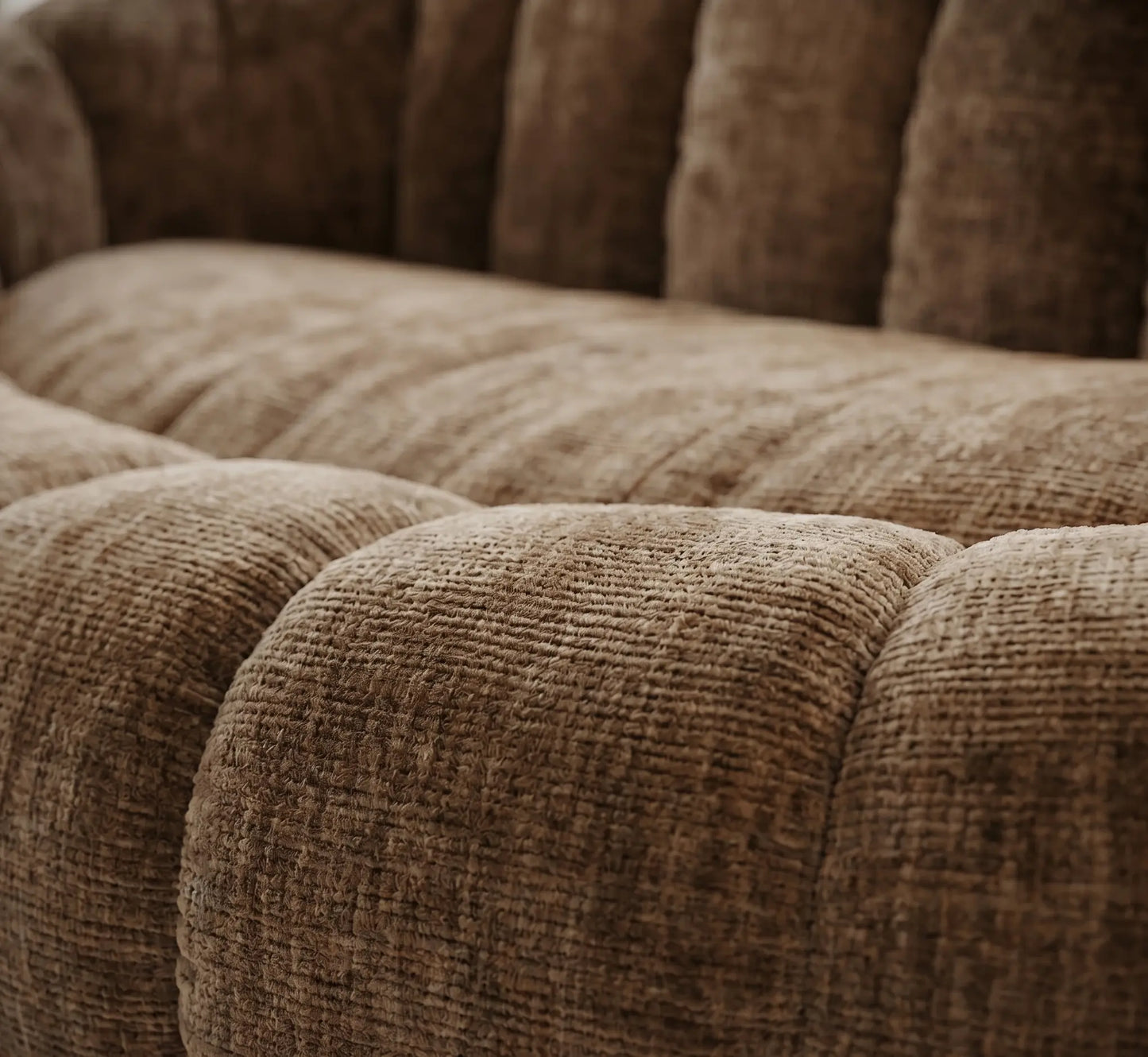 Gros plan sur les courbes capitonnées et la texture du tissu chenille beige sable d'un canapé design, mettant en valeur le relief moelleux et la qualité des fibres.