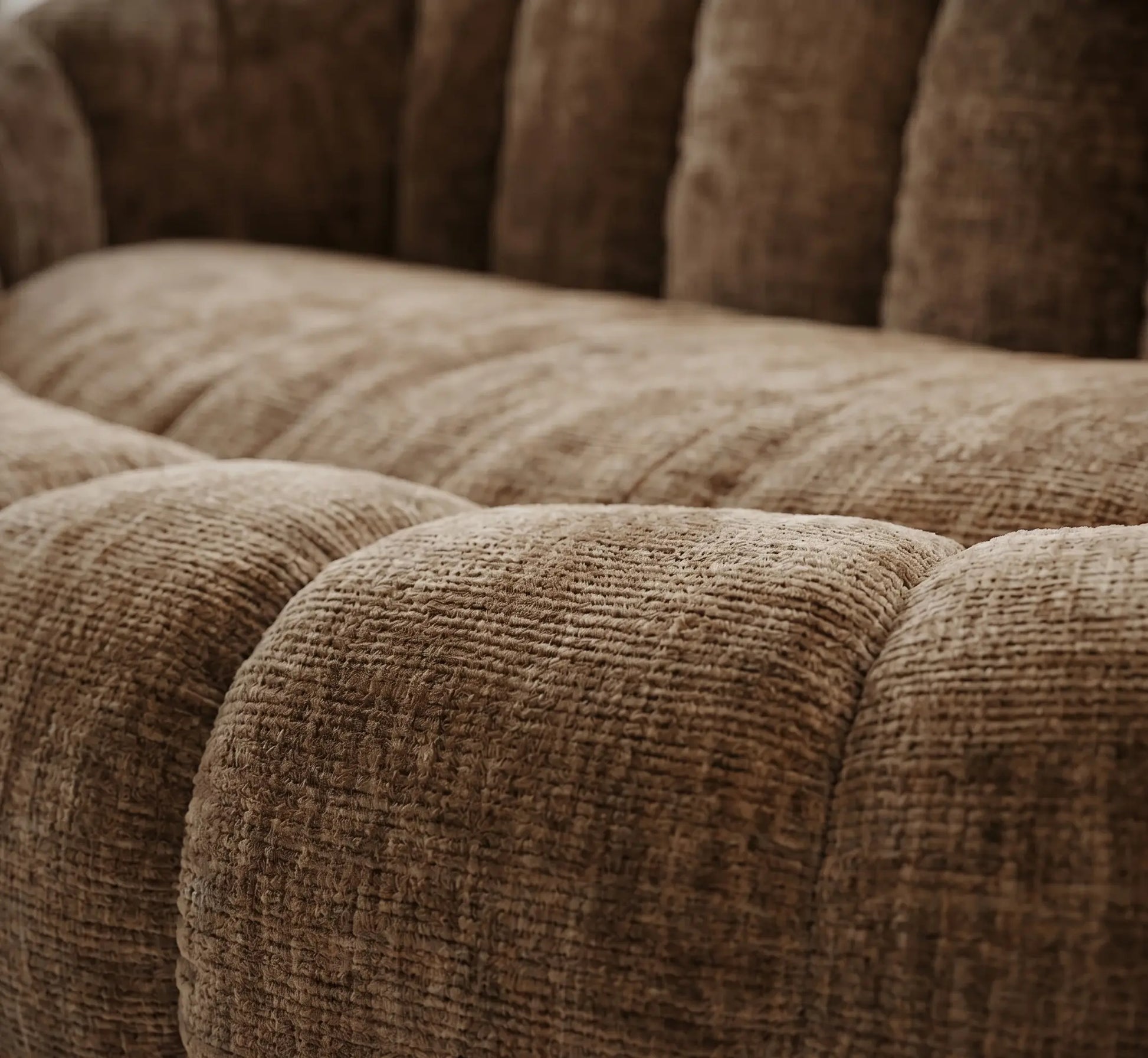 Gros plan sur les courbes capitonnées et la texture du tissu chenille beige sable d'un canapé design, mettant en valeur le relief moelleux et la qualité des fibres.