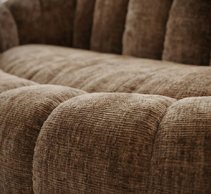 Gros plan sur les courbes capitonnées et la texture du tissu chenille beige sable d'un canapé design, mettant en valeur le relief moelleux et la qualité des fibres.